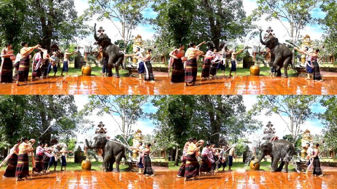 慢动作泼水节——美丽的女人和男人穿着传统的泰国服装，在寺庙背景上用大象泼水