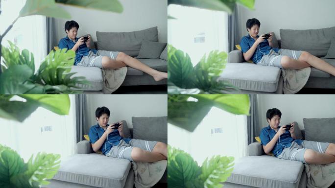 亚洲男孩在家里靠窗的沙发上玩手机游戏，生活方式理念。
