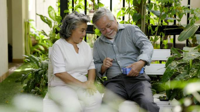 年迈的丈夫在家里用爱的礼盒给妻子惊喜。在结婚纪念日期间。老夫妇微笑着拥抱。