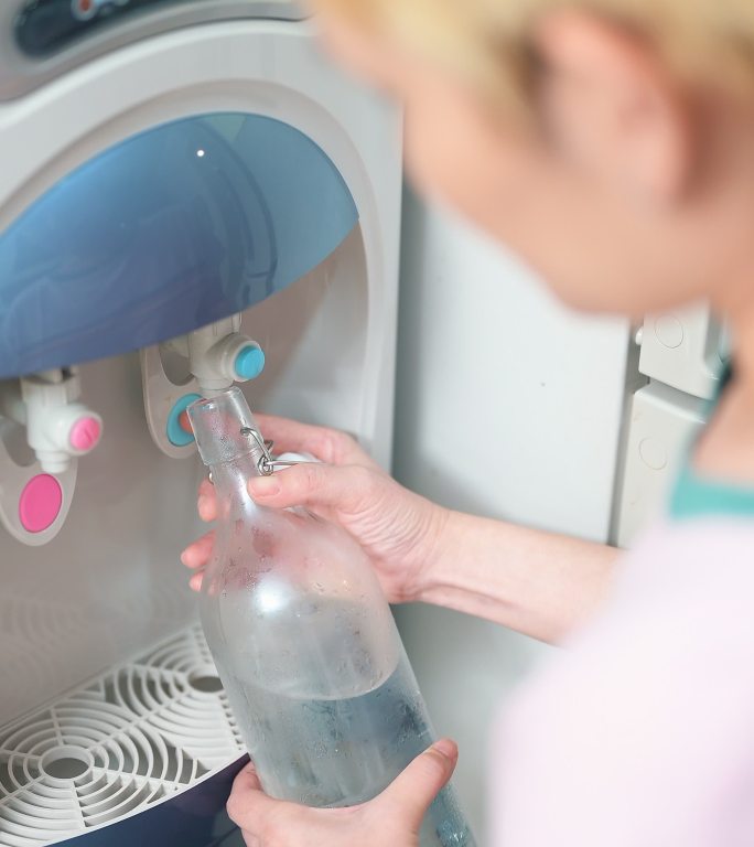 女人在家里用净水器用玻璃瓶装水