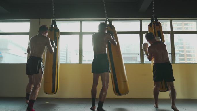 低角度后视极限运动亚洲男子泰拳拳击手连续打沙袋一起在健身俱乐部练习