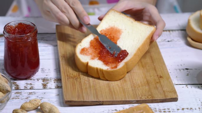 特写镜头，一名女子拿着刀在面包上撒草莓酱。