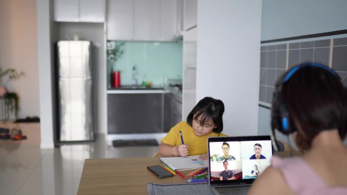 亚裔华裔女商人在家工作视频通话。女儿在餐桌上做作业