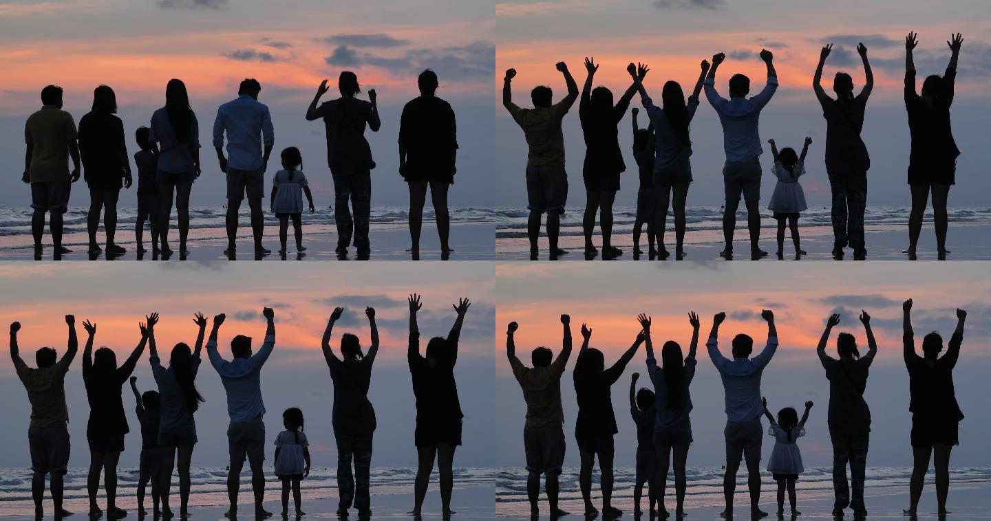 后视图，在剪影中，一个由八个人组成的多代人家庭在仰望风景的同时向空中举起双臂，张开双臂在日落时分的海