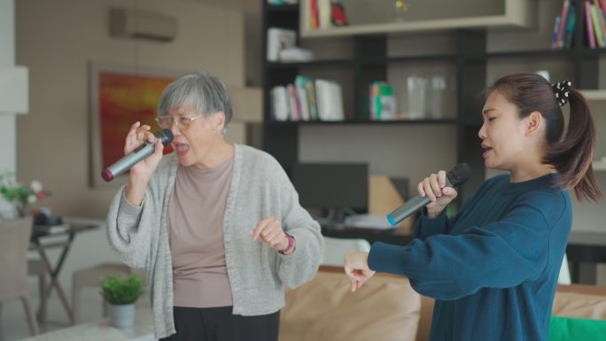 在周末的休闲活动中，亚裔华裔老妇人和女儿在客厅唱卡拉OK跳舞