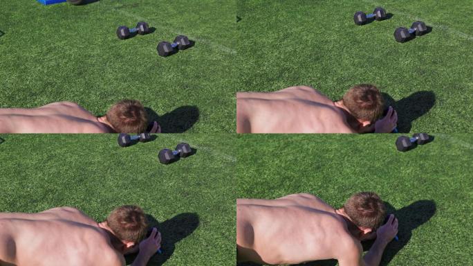 赤膊上阵的男子躺在草地上，架设摄像机拍摄他的运动