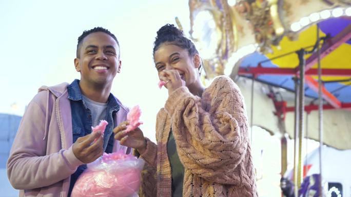 年轻的黑人夫妇在狂欢节上吃棉花糖，大笑