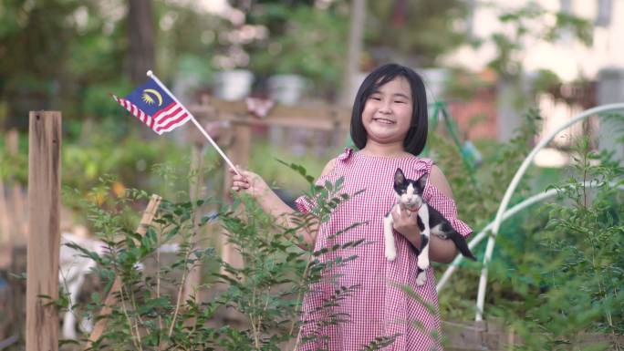 一名亚裔中国女孩，她的宠物猫在自家农场挥舞国旗