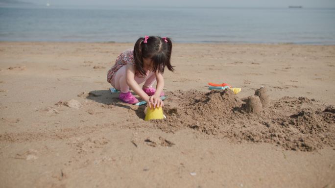 在夏日海滩上建造金沙城堡的年轻女孩