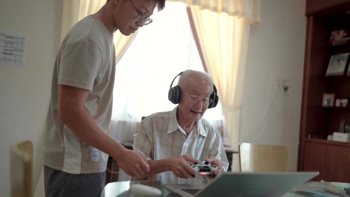 亚裔中国祖父在家里玩孙辈教的网络游戏。