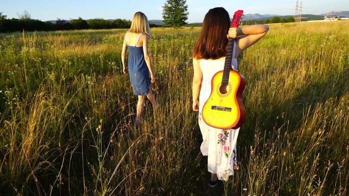 两个年轻女子拿着吉他走在草地上