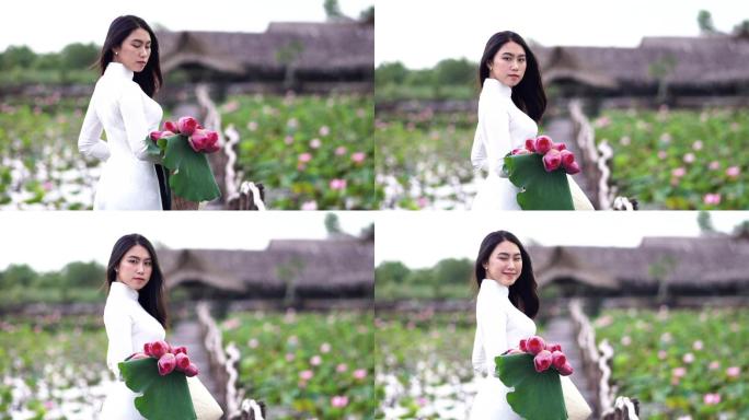 4K慢镜头FHD拍摄了一幅美丽的越南女子手持粉色莲花，在越南大莲花湖木桥上微笑的画面，这是一个亚洲或
