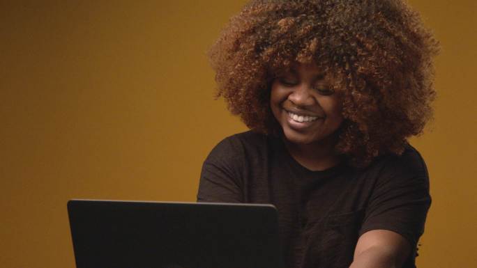 慢镜头工作室拍摄了一位年轻、自信、美丽、专业、快乐的非裔美国女性在笔记本电脑上打字，担任前台接线员、