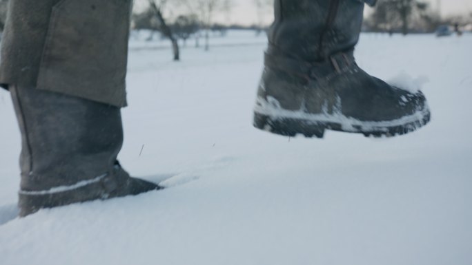 一个男人的靴子在白雪覆盖的田野里行走的特写镜头