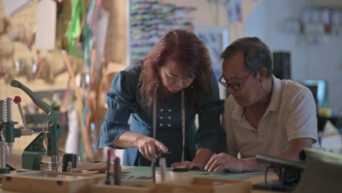 一对亚裔华裔老夫妇在工作室里制作手工皮革表带