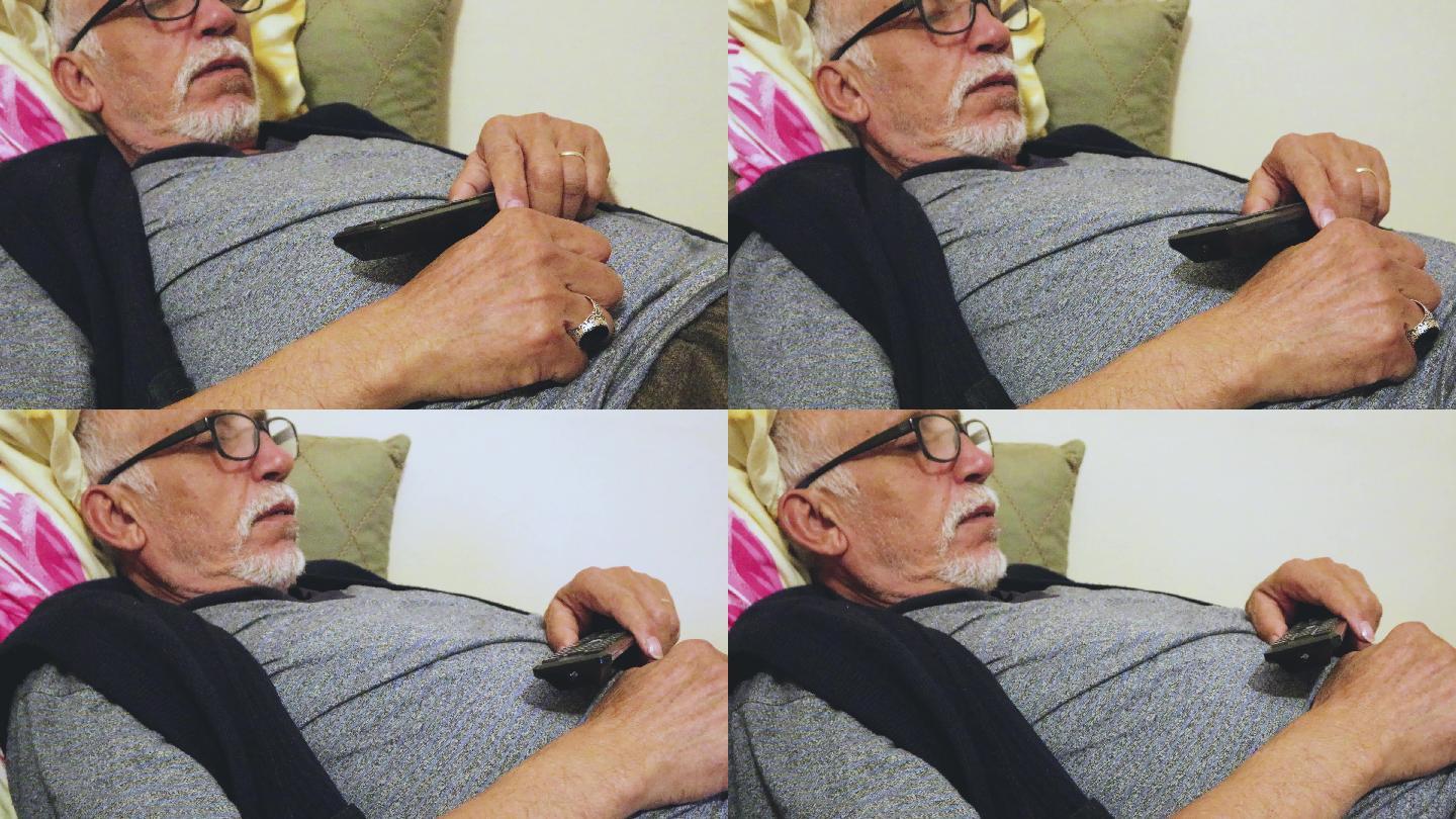 老人一边看电视一边用遥控器睡着了