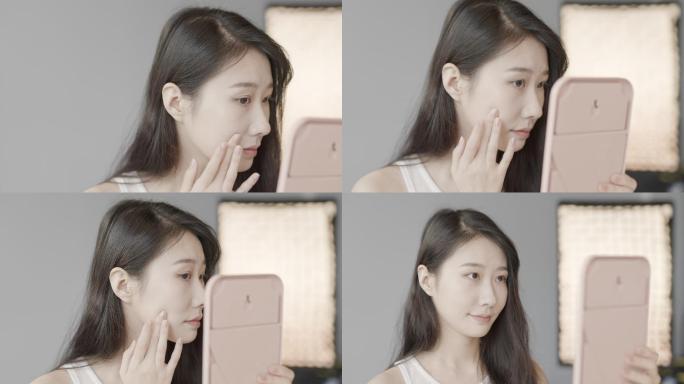 美丽的长发韩国女性在镜子里检查粉刺，早上护肤，慢动作，明亮的房间