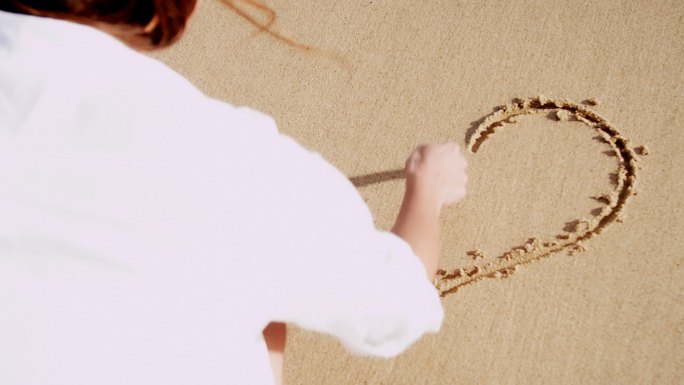 在沙子上画心形的女人