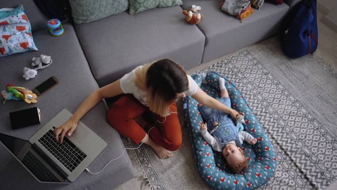 年轻的单身母亲在家工作，她的儿子躺在她身边