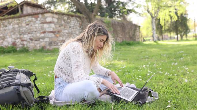 阳光明媚的春日，一位年轻女子在城市公园里用笔记本电脑工作
