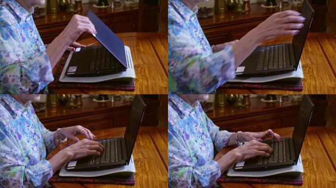 一位在家工作的拉丁美洲资深女士的手，坐在餐桌旁的笔记本电脑上