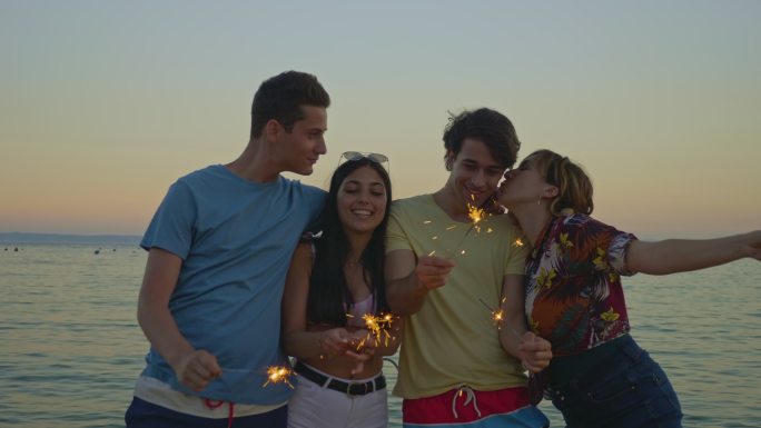 年轻的朋友们拿着照明弹在海滩上玩日落