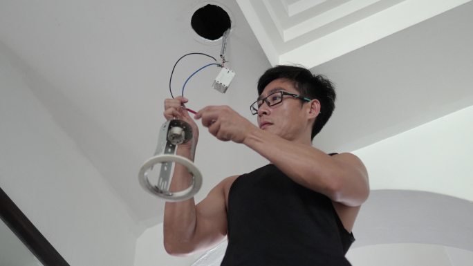 亚裔中国成年男子电工盖住电缆，在一家家装店安装电灯