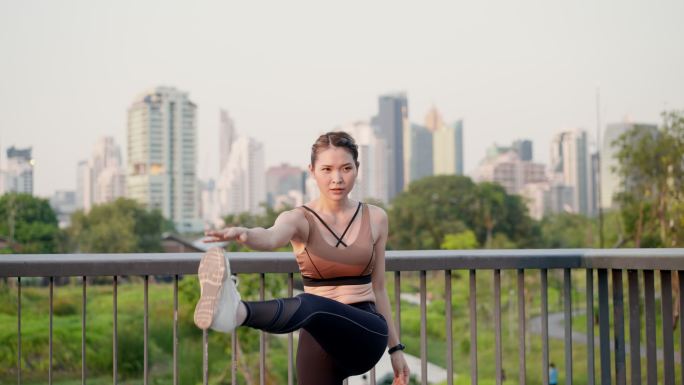 亚洲美丽的中年女性，穿着运动服，早上在城市公园的人行天桥上锻炼后，通过伸展腿部和手臂肌肉，达到完美的