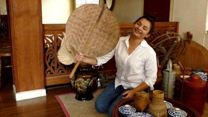 在一座古老的木屋里，一位手持泰国传统竹扇的亚洲女子