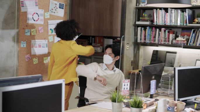 黑人女商人肘部磕碰预防2019冠状病毒疾病早上在办公室与同事打招呼，戴着防护面罩，练习社交距离以确保
