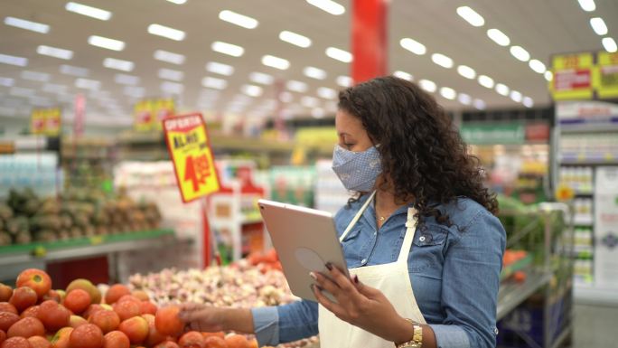 一名戴着口罩的女子在超市用数码平板电脑检查蔬菜