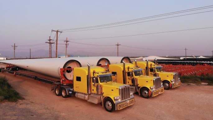 风力涡轮机由超长平板半拖车卡车从墨西哥运过边境，并排停放