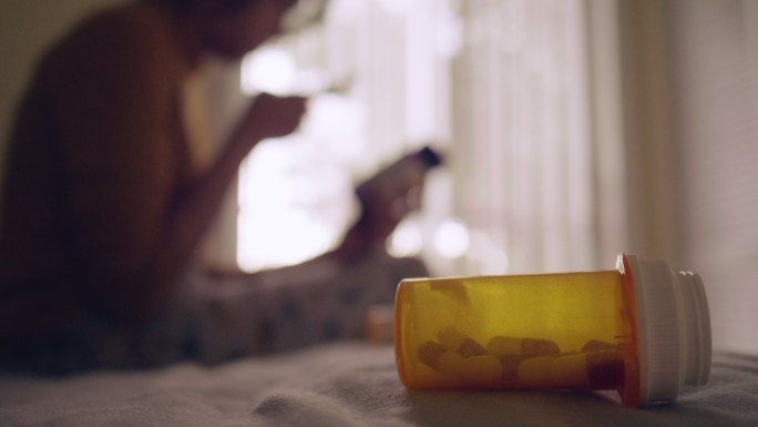 年轻的亚洲女人拿着药瓶，在卧室里用手机聊天