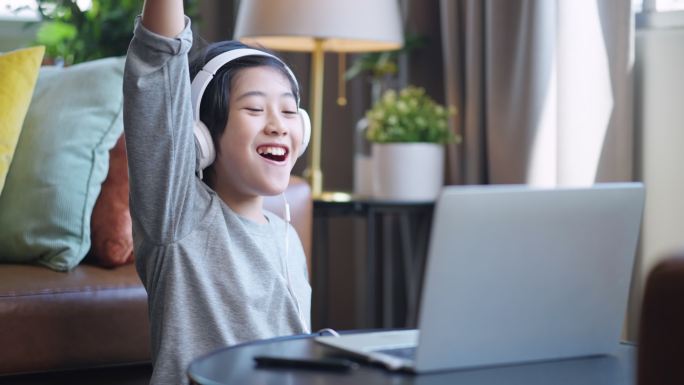 周末假期，亚洲男孩戴着耳机，玩着笔记本电脑游戏，坐在客厅的地板上玩着开心的游戏，儿子独自玩着移动设备