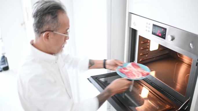高角度亚裔中国高级男子早上在厨房用微波炉解冻肉类，准备早餐