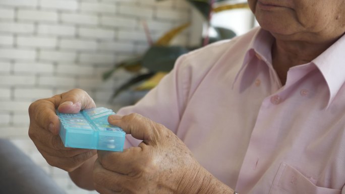 一名亚洲老人在家里仔细地将处方药分类到药丸管理器中。