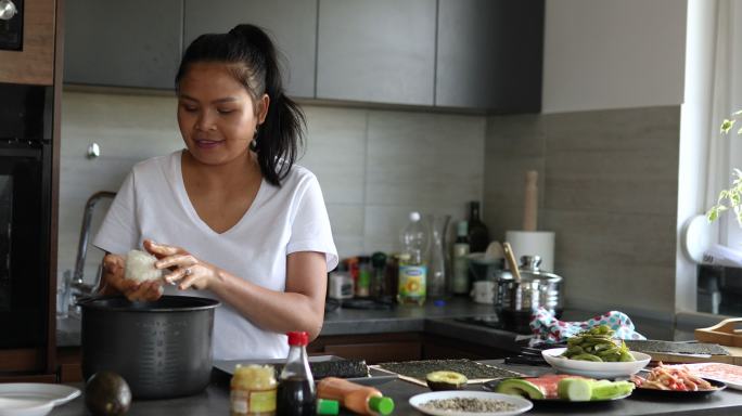 一名泰国女子，一名寿司厨师，将寿司米饭放在海苔上，准备传统寿司卷作为午餐