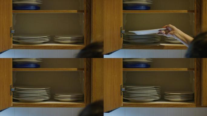 一名白人女性用手将各种大小的干净盘子放入一个开放式厨房橱柜