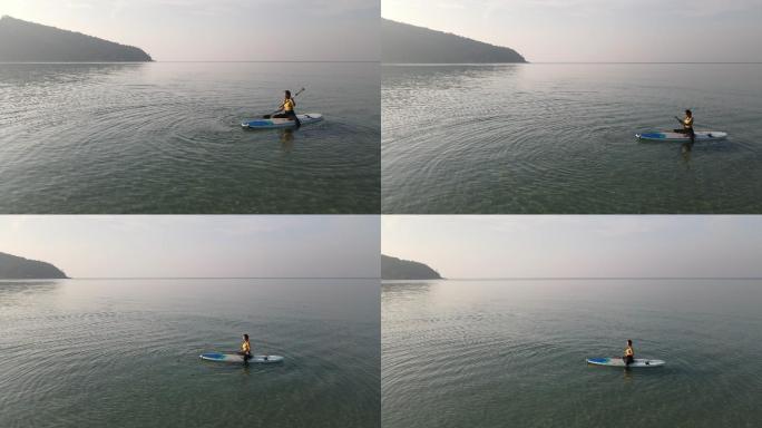 早上在划桨板上练习瑜伽的鸟瞰图，柔和的阳光照射在海面上。