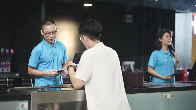 亚裔中国年轻男子在电影院用非接触式支付购买爆米花和饮料