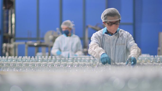 2名中国亚裔饮用水厂生产线工人，戴着PPE，每天检查水瓶