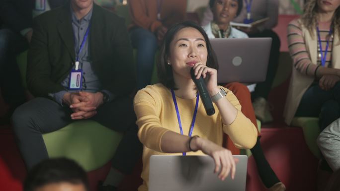 年轻漂亮的亚洲女人在一个满是观众的房间里参加商务会议时问问题