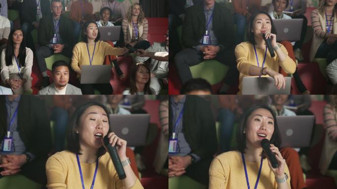 年轻漂亮的亚洲女人在一个满是观众的房间里参加商务会议时问问题