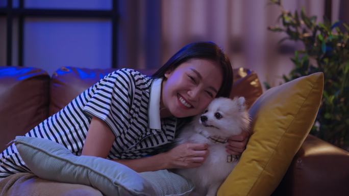 笑容可掬的亚洲女性坐在沙发上，拥抱着小狗，与狗主人和奇瓦瓦·拉普多普一起在家度过周末快乐的假期
