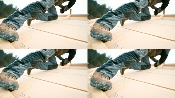 一名工人的脚站在屋顶板条上，一边用螺丝钉穿过屋顶上的木梁