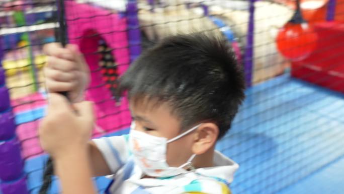 亚洲小孩戴着医用口罩在室内游乐场玩耍。保护、创造力和学习的概念