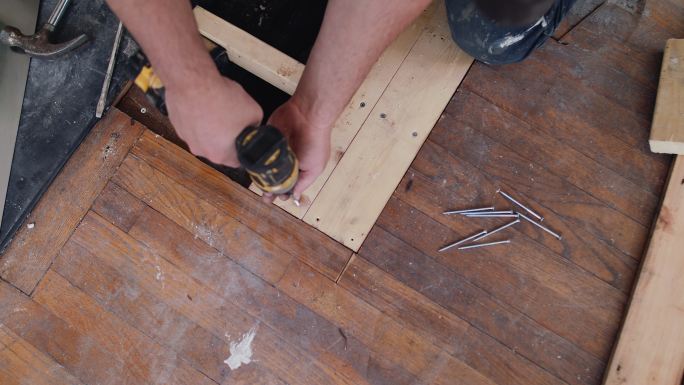 男性建筑工人使用电钻安装地板