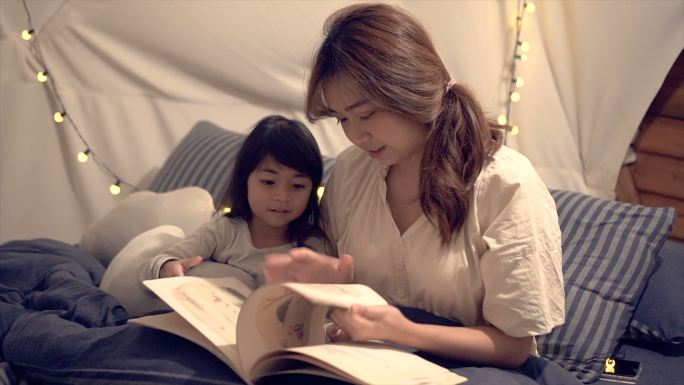 一位母亲晚上露营时在帐篷里给女儿读故事。