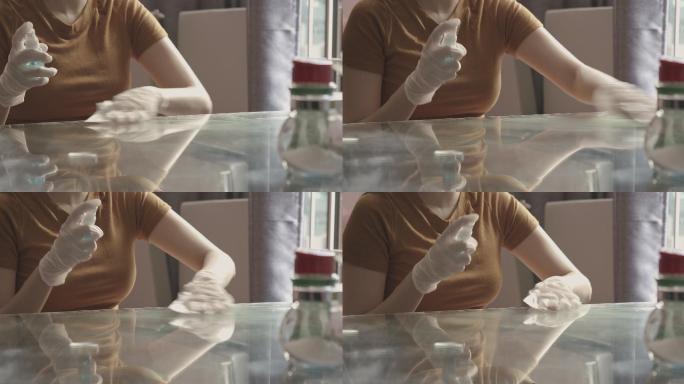 新冠肺炎19：戴手套的亚洲女性，在玻璃桌上喷洒酒精清洁和消毒表面。女性在封锁情况下使用消毒消毒剂或一