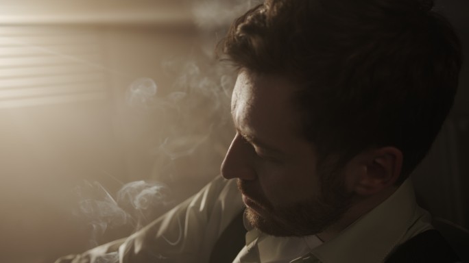 一个穿着衬衫的孤独商人在黑暗的房间里抽雪茄